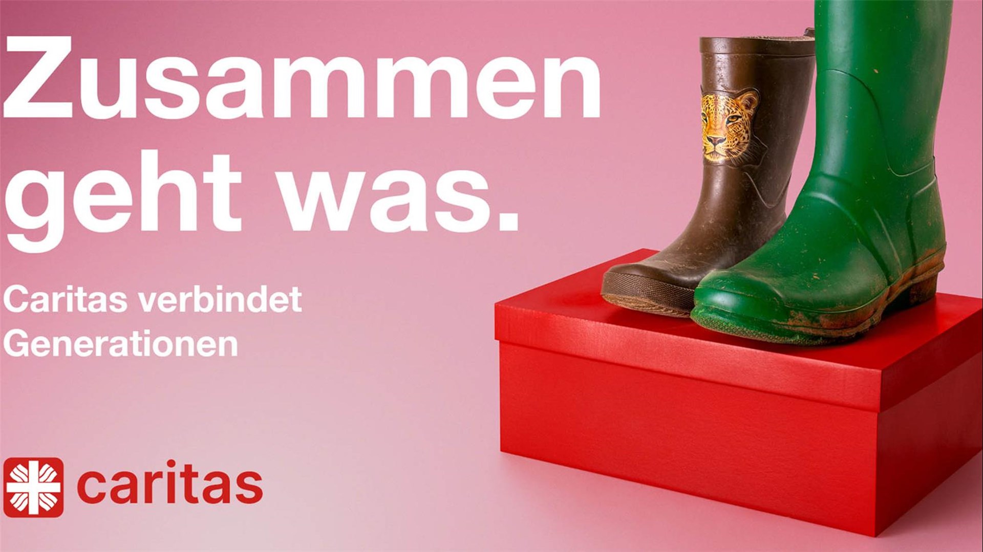 Auf einem roten Schuhkarton sind vor einem rosa Hintergrund ein Paar Gummistiefel zu sehen. Der linke Schuh ist ein brauner Kindergummistiefel mit einem Tigerkopf in kleiner Schuhgröße, der rechte ein hoher grüner Gummistiefel in großer Schuhgröße. Darüber steht das Kampagnenmotto: Zusammen geht was. Caritas verbindet Generationen.